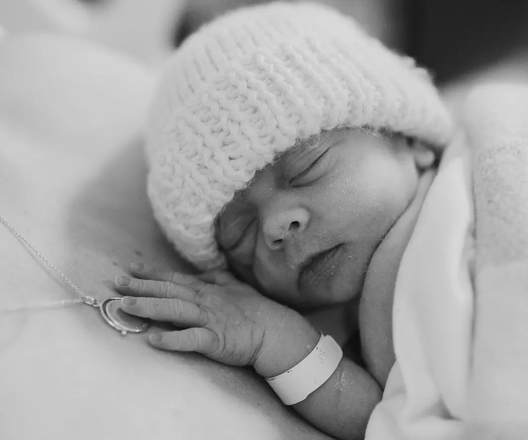 Newborn baby sleeping with a knitted hat on, wrapped in a blanket.